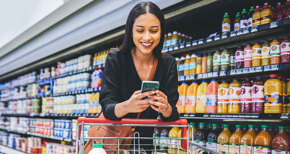 Woman shopping at grocery store and smiling at phone